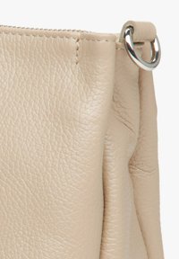 Beige leren tas met een gestructureerd oppervlak, voorzien van een zilveren metalen ring en een geplooid ontwerp langs de bovenrand.