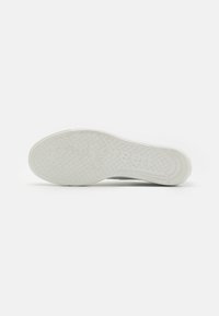Weiße Sneaker-Sohle aus strukturiertem Gummi, mit einem gepunkteten Muster und eingeprägtem Markennamen. Abgerundete Form und geschwungene Kanten.