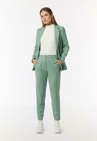 Light green, tailored suit with a structured blazer and slim-fit pants. Paired with a cream cable-knit sweater and white sneakers.