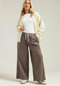 Krämfärgad ribbad klänning över vit topp, tillsammans med bruna randiga vida byxor och vita sneakers; avslappnad passform, elastisk midja med dragsko.