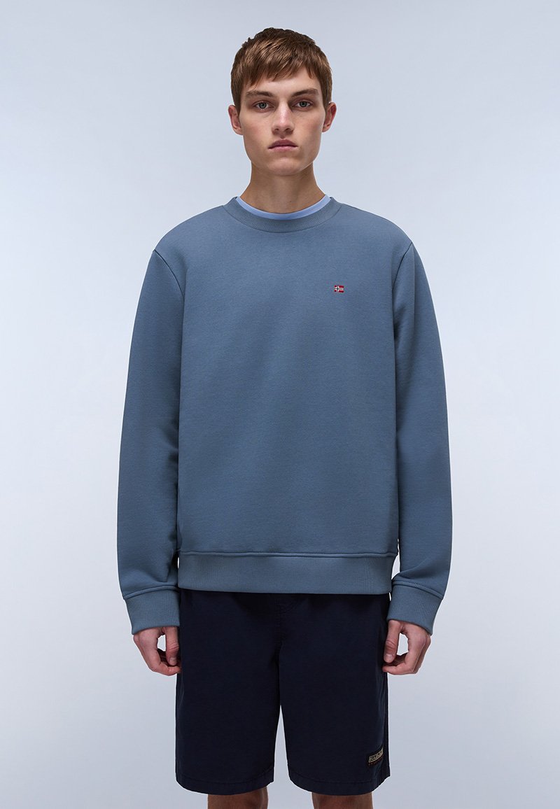 Blå crewneck genser laget av bomullsblandingsstoff, med ribbestrikket hals og subtil logo-detalj. Kombinert med mørke shorts.