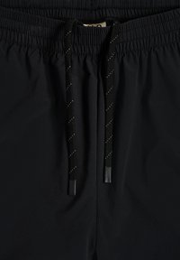 Schwarze Shorts mit elastischem Bund und schwarzem Kordelzug, versehen mit weißen reflektierenden Streifen und schwarzen Kunststoff-Spitzen.