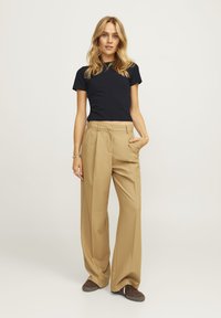 Zwarte fitted t-shirt gecombineerd met beige wijde broek met hoge taille en zijzakken. Gestyled met bruine sneakers.