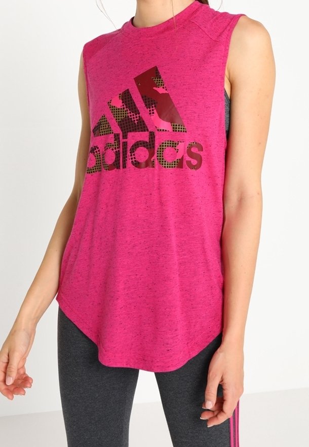 Personne portant un débardeur rose Adidas avec un logo noir et rose, associé à des leggings gris foncé avec des rayures roses.