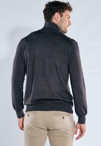Dark gray turtleneck sweater with long sleeves and ribbed hem, paired with light beige trousers featuring buttoned back pockets.