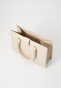Beige handbag with a structured design, smooth texture, two top handles, and gold-tone hardware. Zippered interior compartment visible.
