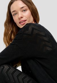 Zwart gebreid outfit met een visgraatpatroon, met een getextureerde weef. De stof lijkt lichtgewicht en ademend te zijn.