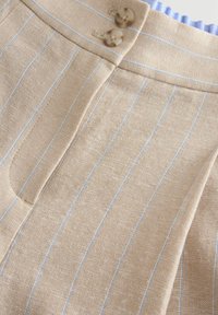 Beige lněná látka s světle modrými pruhy, s pasem se dvěma hnědými knoflíky a bočním kapsovým detailem.