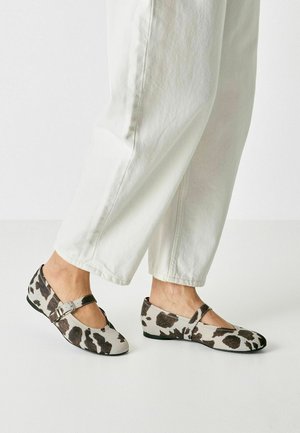 Bailarinas con un estampado de vaca en beige y marrón, cuentan con una correa con hebilla y una puntera redondeada, combinadas con pantalones blancos de pierna ancha.
