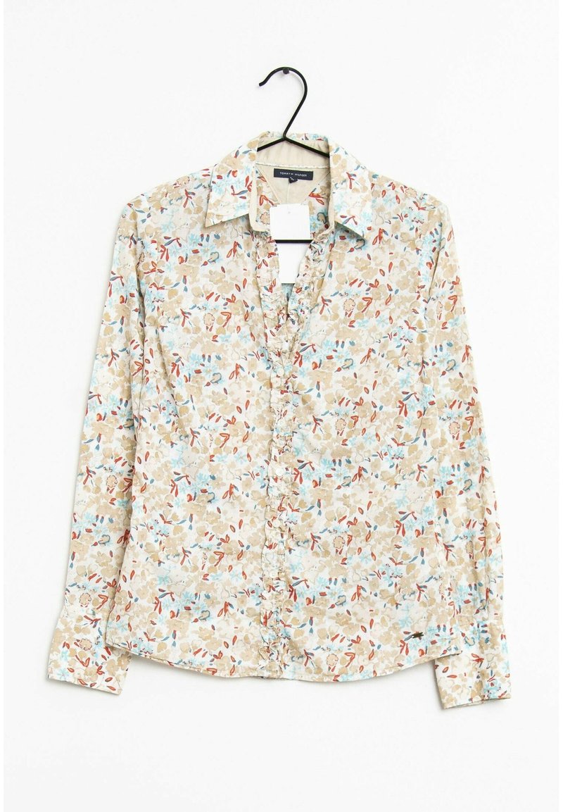 Camisa de botones con estampado floral sobre un fondo beige con patrones florales en azul y rojo. Mangas largas, cuello y dobladillo redondeado.