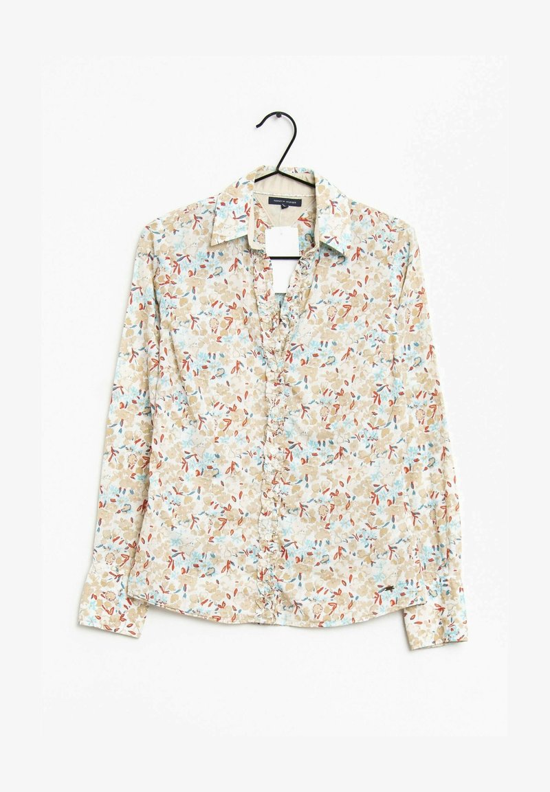Camisa de botones con estampado floral sobre un fondo beige con patrones florales en azul y rojo. Mangas largas, cuello y dobladillo redondeado.