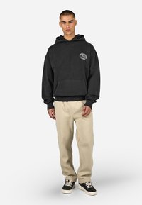 Čierna mikina s kapucňou a predným vreckom s grafickým logom. Skombinovaná s krémovými nohavicami a čierno-bielymi teniskami.