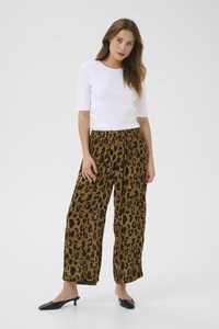 Pantalons larges à imprimé léopard marron en tissu léger, associés à un t-shirt blanc cintré et des mules à talons noirs.