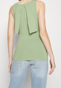 Grön ärmlös topp i mjukt tyg, med ett löst bakpanelhäng. Lätt och figurnära design med rund halsringning och slät textur.