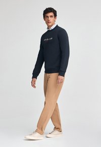 Sudadera navy con logo, pantalones caqui y zapatillas blancas. Textura suave, diseño de cuello redondo y silueta ajustada.