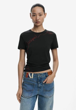 Black cotton t-shirt featuring red embroidered text along the side. Fitted design with short sleeves and crew neckline. Paired with blue denim jeans.