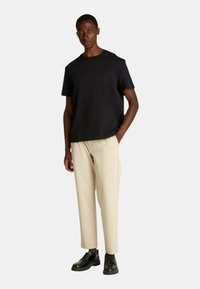 Camicetta nera a maniche corte con finitura testurizzata, abbinata a pantaloni beige a sigaretta e scarpe nere con lacci. Silhouette semplice e moderna.