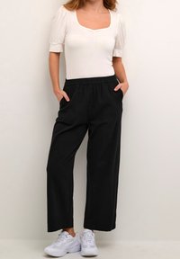 Black wide-leg pants with an elastic waistband and side pockets, paired with a white fitted top and white sneakers. Smooth texture.