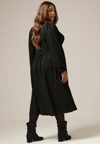 Vestido negro texturizado con mangas largas y cintura ajustada, que cae a media pantorrilla. Se lleva con botas de ante negras hasta la rodilla.