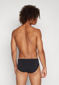 Schwarze Schwimmshorts mit glatter Textur, featuring einen niedrigen Bund und einem enganliegenden Design, von hinten betrachtet, ohne sichtbare Muster.