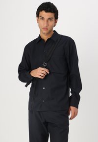 Navy long-sleeve button-up shirt with a single chest pocket, paired with matching pants; smooth texture, classic design, minimal accents.