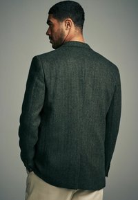 Dunkelgrüner Fischgrät-Blazer mit strukturierten Schultern und Reverskragen, aus strukturiertem Stoff mit einem einzelnen Rückenschlitz.