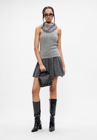 Maglione grigio con collo a cappuccio, gonna grigia plissettata, borsa nera decorata e stivali neri lucidi fino al ginocchio. Elementi di design semplici e moderni.