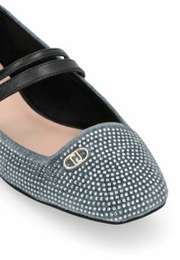 Grijze suede platte schoen met zwarte dubbele band, versierd met zilveren studs en een gouden hardware logo op de spitse neus.