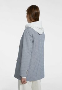 Rutigt blazer i blått och vitt, med dubbelknäppning, huva och silverfärgade knappar. Mjuk tyg med avslappnad passform.