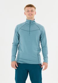 Vaaleansininen pitkähihainen neule, jossa on puolivetoketjukaulus, litteät saumat ja istuva malli, yhdistettynä tummansinisiin shortseihin.