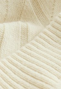 Cream-colored knit fabric featuring a mix of ribbed and textured patterns. Soft, fuzzy texture with visible fibers, enhancing warmth.