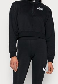 Svart cropped sweatshirt med halvvipp, texturerad övre panel och broderad logotyp. Matchad med svarta leggings med en vit swoosh-design.