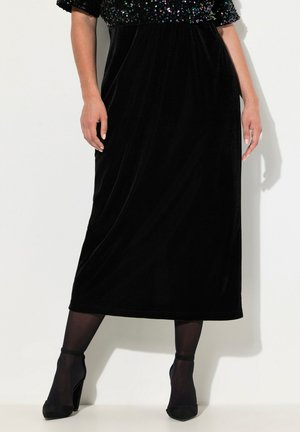 Vestido de terciopelo negro con mangas cortas de lentejuelas y una silueta suelta, hasta la rodilla, combinado con zapatos de tacón alto negros y medias.