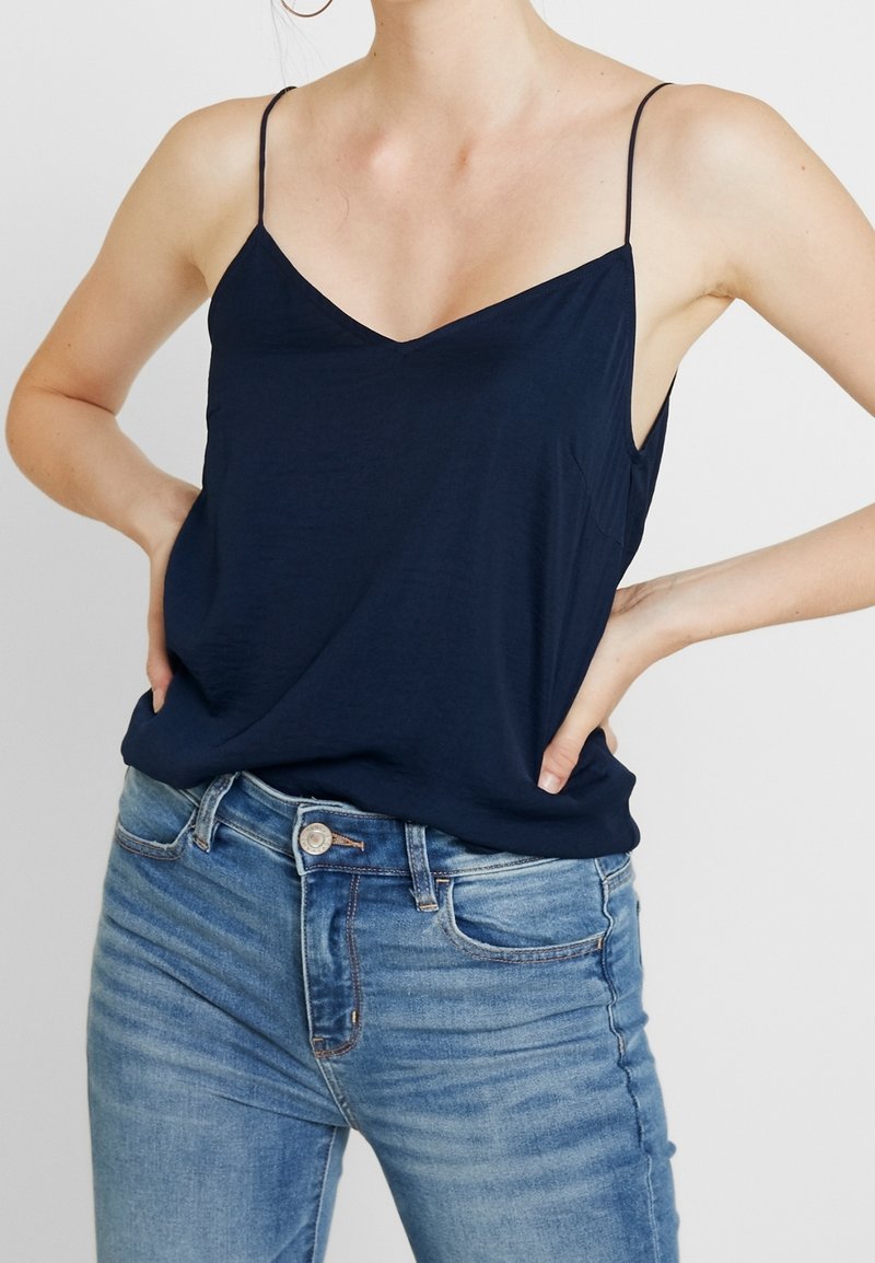 Marinblå ärmlös topp med V-hals, mjukt tyg och avslappnad passform, kombinerad med ljusblå jeans med knappstängning och framfickor.