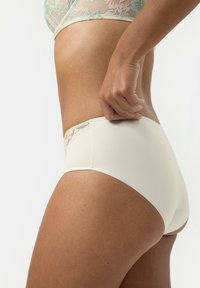 Witte short met kantafwerking in mintgroen, van opzij weergegeven. Soepele textuur met een naadloos ontwerp en een minimalistische snit.
