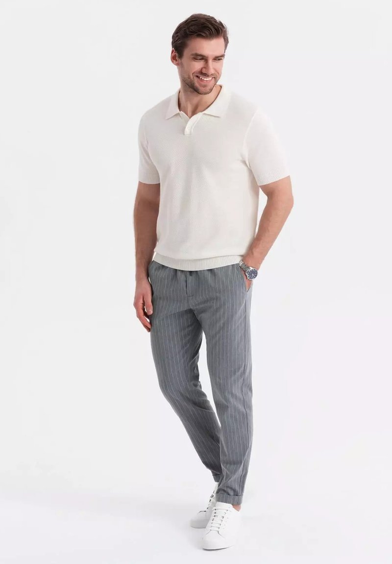 Lehká krémová polokošile s krátkým rukávem a texturovanou látkou, v kombinaci se šedými proužkovanými kalhotami a bílými teniskami.