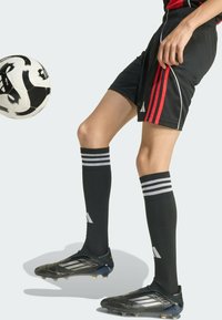 Svarta fotbollsshorts med röda ränder, svart och vit fotboll, svarta fotbollsskor med silverdetaljer och knähöga svarta strumpor med vita ränder.