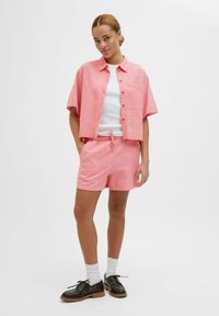 Roze en witte gestreepte korte mouwen shirt, gecombineerd met bijpassende shorts met trekkoord, voorzien van een zak, gedragen met donkere schoenen en witte sokken.