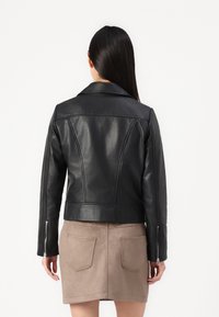 Svart lær cropped jakke med klippete krage, glidelåsfester på ermene og buede sømmer, kombinert med en tan suede skjørt med baklommer.