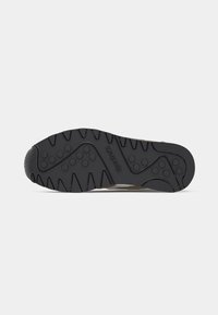 Čierna podrážka tenisky s textúrovaným vzorom, obsahujúca kruhové gripy a diagonálne línie. Embosované logo "Reebok" na boku.