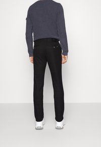 Czarne spodnie w kratę o dopasowanym kroju, z dwoma tylnymi kieszeniami i dyskretną metką marki w pobliżu talii, zestawione z teksturowanym granatowym swetrem.