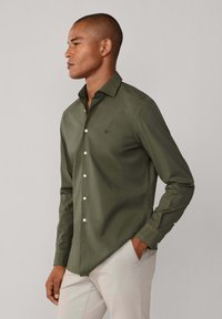 Olijfgroene lange mouwen blouse met knopen en een gestructureerde kraag, voorzien van witte knopen en een subtiel geborduurd logo op de borst.