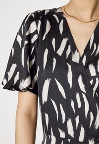 Robe noire à motif coups de pinceau blancs, avec un décolleté en V et des manches courtes bouffantes, réalisée en tissu lisse avec une légère brillance.