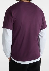 Tričko s krátkým rukávem z tmavě fialové bavlny, vrstvené přes bílé tričko s dlouhým rukávem, s kulatým lemem a volným střihem.