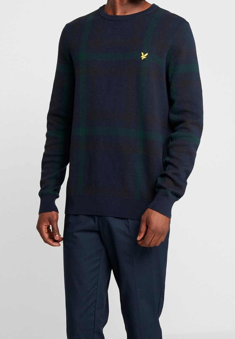 Dunkelblauer Pullover mit einem grün-braunen Karomuster, Rundhalskragen, langen Ärmeln und einem kleinen gelben Logo auf der Brust.