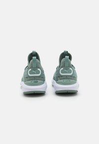 Zapatillas deportivas verdes con parte superior de tela texturizada, suela blanca en contraste y talón acolchado. Presentan el logo y una lengüeta en la parte trasera.