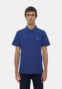 Polo shirt blu scuro realizzato in tessuto liscio, con colletto classico, maniche corte e un piccolo logo sul petto a sinistra.
