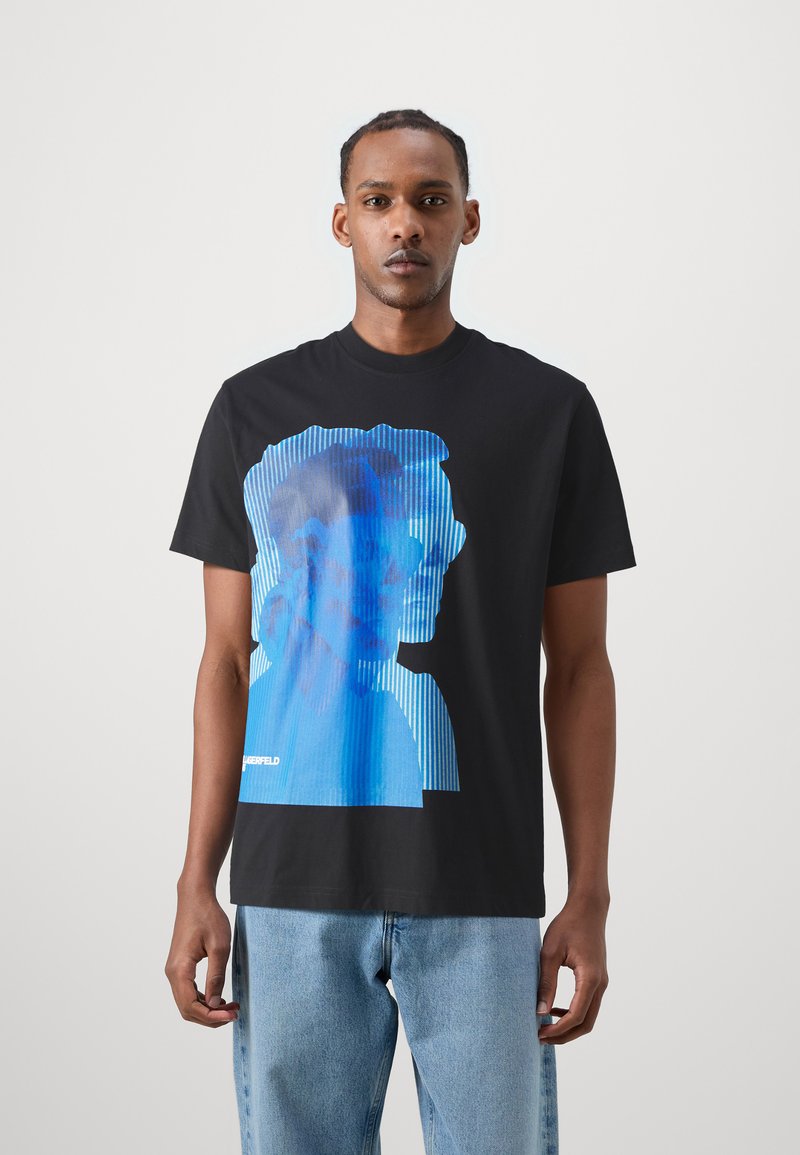 T-shirt in cotone nero con una grande grafica blu di un volto con linee verticali. Collo rotondo e maniche corte. Vestibilità casual.