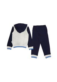 Tuta a due pezzi blu navy e bianco, caratterizzata da una giacca con cappuccio, polsini e orlo a costine, e pantaloni abbinati con accenti a righe blu.