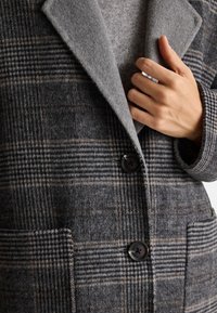 Cappotto a quadri grigio realizzato in un mix di lana testurizzata, caratterizzato da un ampio colletto, due tasche frontali e chiusura con un solo bottone di colore nero.